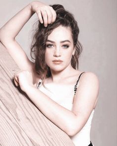 a beautiful young woman leaning against a wooden wall with her hand on her head and looking at the camera