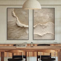 two paintings are hanging on the wall above a dining room table with chairs and a lamp