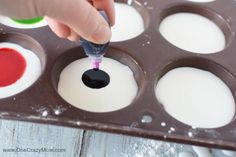 a person is dipping paint into a muffin tin with white and red circles on it