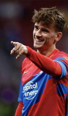 two soccer players in red and blue uniforms are pointing to the sidelines with their hands together