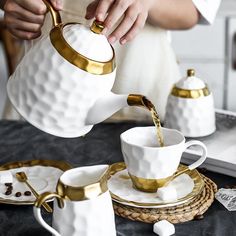 a person pouring water into a white coffee cup on top of a black and gold plate