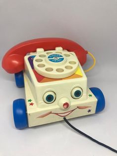 an old fashioned toy phone with eyes on it's face and hands holding a cord