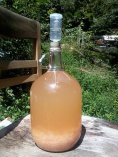 a glass bottle filled with liquid sitting on top of a wooden table next to a park bench