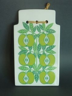 a white cutting board with green apples and leaves on it, hanging from a hook