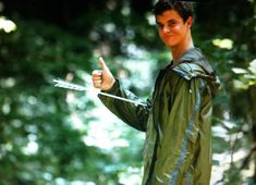 a young man in a green jacket holding a pair of scissors and pointing at something