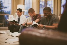 three men are sitting on the couch reading books and laughing at each other's company