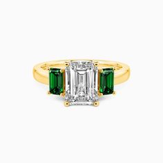 an emerald and diamond three stone ring with two diamonds on each side, set in yellow gold