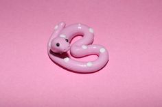 a pink snake brooch with white dots on it's head and tail, sitting on a pink surface