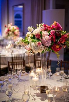 the centerpieces on this table are filled with pink and white flowers, greenery, and candles