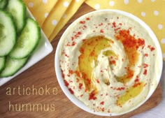 a bowl filled with hummus sitting on top of a table next to sliced cucumbers