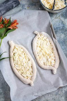 two uncooked pizzas sitting on top of a piece of paper next to flowers