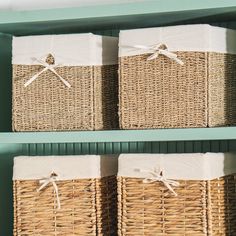 two wicker baskets with white linens tied to them are sitting on green shelves