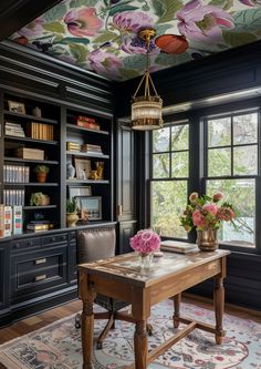 a desk with flowers on the ceiling and bookshelves in front of it, next to a large window