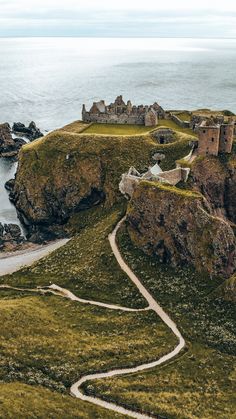 an aerial view of a castle on top of a hill near the ocean with a path leading to it