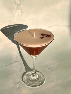 a drink in a martini glass with a candle on the rim and garnished with cherries