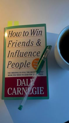 the book how to win friends and influence people is next to a cup of coffee