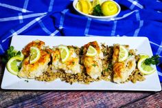 a white plate topped with chicken and rice covered in lemons next to a bowl of lemon wedges