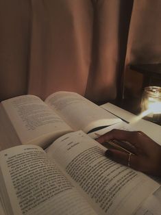 an open book on a table next to a candle and some books with writing utensils