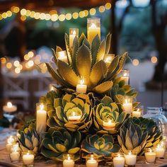 an arrangement of candles and succulents are arranged on a table with lights in the background