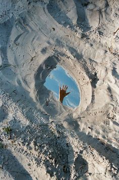 a person's hand sticking out of the sand in front of a small puddle