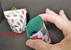 a hand is holding an origami cup in front of another one with christmas decorations on it