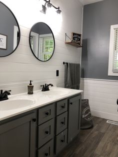 a bathroom with two round mirrors above the sinks and gray cabinets, along with white walls