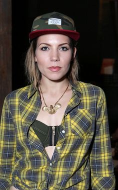 a woman wearing a green and yellow plaid shirt with a hat on her head is posing for the camera