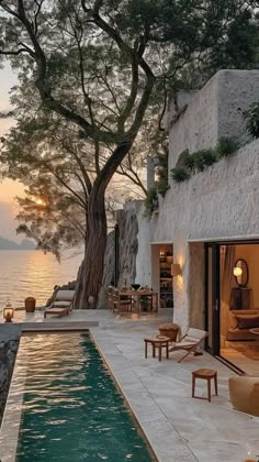 an outdoor swimming pool with chairs and tables next to the water at sunset or dawn