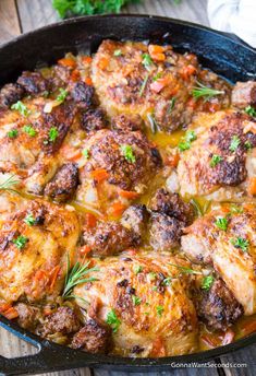 a skillet filled with meat and vegetables on top of a wooden table next to a fork