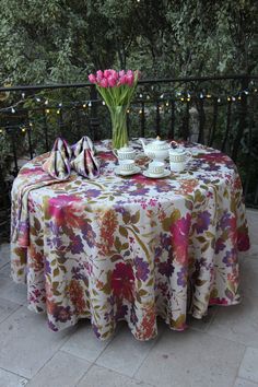 a table with flowers and tea cups on it is set up outside by the fence