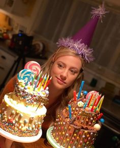 a woman is holding two birthday cakes with candles on them and one cake has many candies all over it