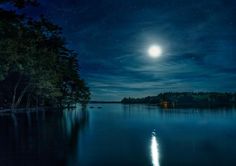 the full moon is shining brightly in the night sky over a body of water with trees