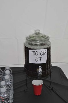 a black table topped with lots of bottles and a jar filled with liquid next to a red cup