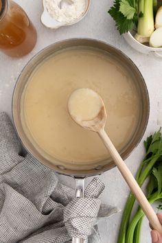 a person holding a wooden spoon over a pot filled with liquid next to other ingredients