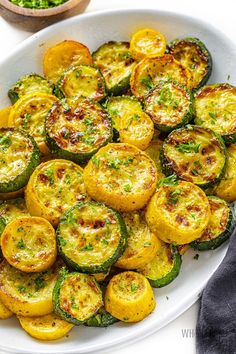 a white platter filled with cooked zucchini and squash on top of a table