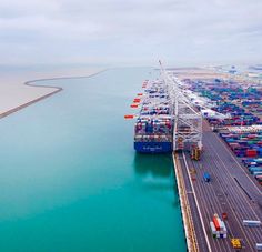 an aerial view of a large cargo ship in the ocean with other ships and trucks