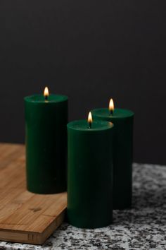 three green candles sitting on top of a wooden board