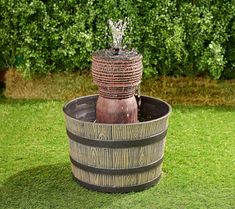 a wooden barrel with water coming out of it in the middle of some green grass