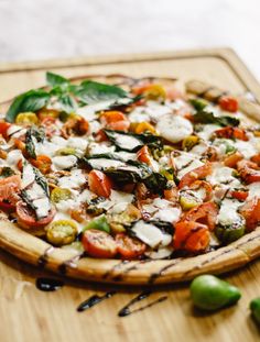 a pizza sitting on top of a wooden cutting board next to green peppers and tomatoes