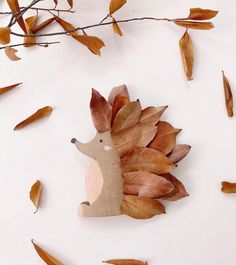 a hedgehog made out of leaves on a white surface with twigs and branches in the background