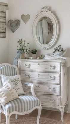 a white dresser sitting next to a chair in a room with a mirror on the wall