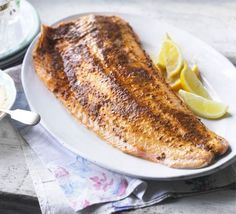 a piece of fish on a white plate with lemons and sauce next to it