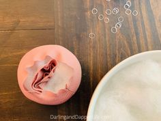 a pink hat sitting on top of a wooden table next to a bowl filled with bubbles