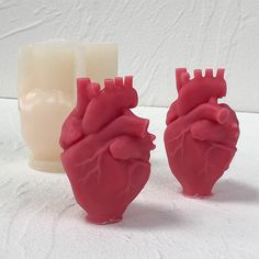 two heart shaped candles sitting next to each other on a white tableclothed surface