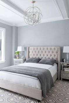 a bedroom with gray walls and white bedding, chandelier above the bed