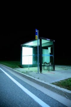 a bus stop sitting on the side of a road at night