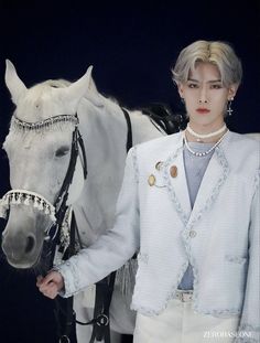 a woman standing next to a horse wearing a white jacket and pearls on it's head