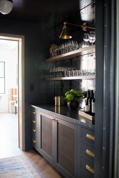 a kitchen with black walls and gold trim on the countertop, wine glasses are lined up on shelves