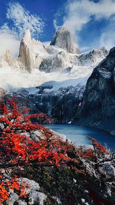 the mountains are covered in snow and red trees with orange leaves on them, near a body of water