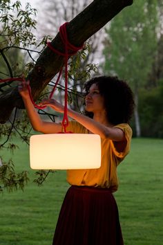 a woman holding onto a light hanging from a tree